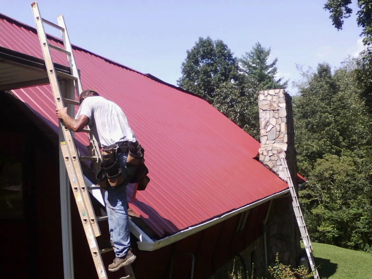 Roofer on a ladder beside a red metal roof and stone chimney in Mammoth Cave