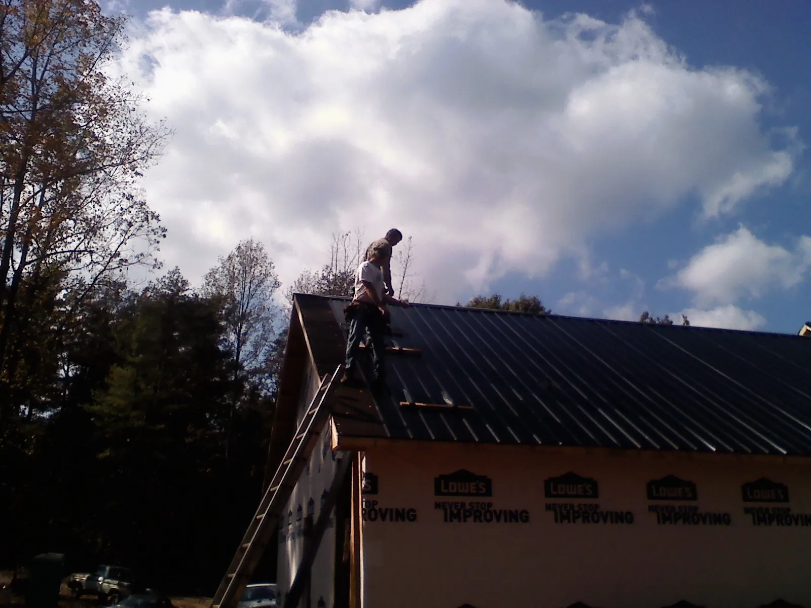 Roofer fastening dark metal panels high against a cloudy sky, from a Roof Inspection job in Mammoth Cave