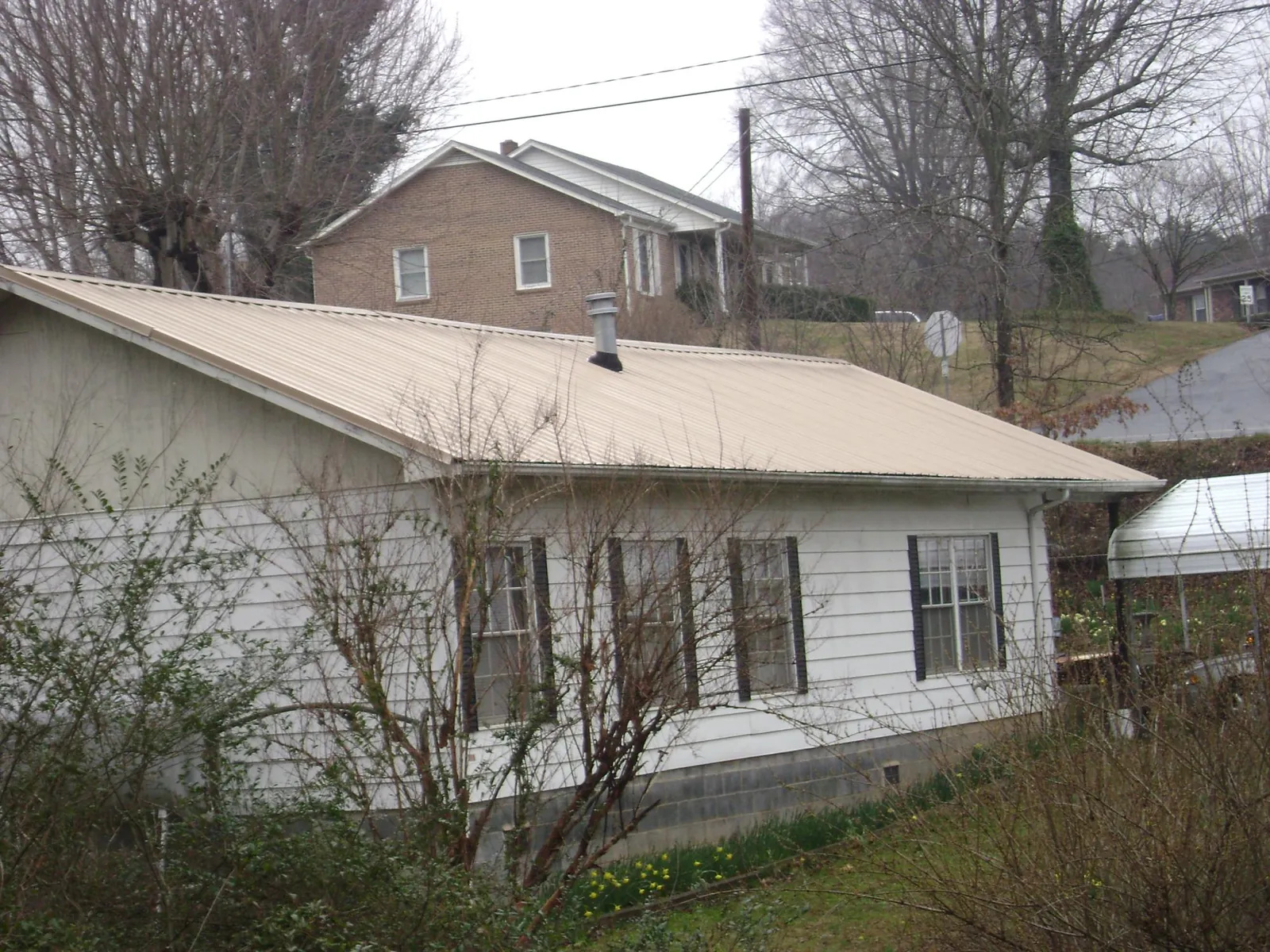 Tan metal roof on a white sided house set into a hillside — Commercial Roofing by Roofing Brothers in Mammoth Cave